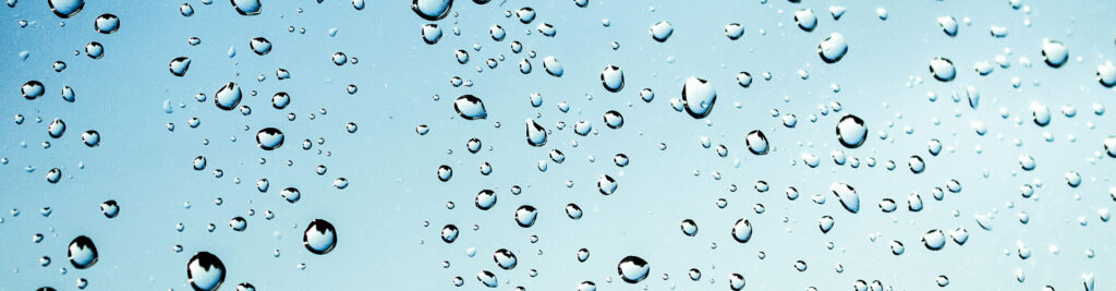 Close-up of water droplets on a glass surface with a pale blue gradient background, forming a refreshing pattern.