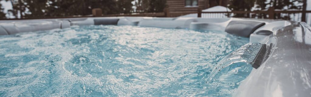 Outdoor hot tub with frothy, bubbling blue water and a wooden fence in the background, hinting at a cold-day setting.