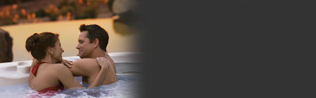 Couple in a hot tub embracing and smiling at sunset outdoors.
