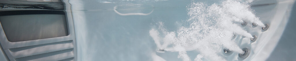 White/gray hot tub interior with multiple silver jets and bubbling water, control panel visible on the left.
