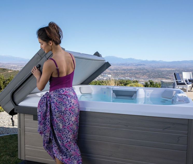 Woman opening hot tub cover - Oregon Hot Tub explains why buying a spa cover during winter is best.