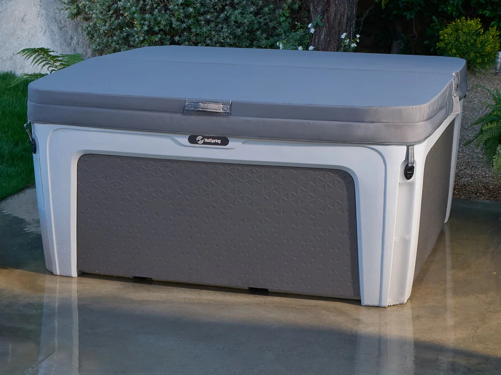 Outdoor hot tub with a gray cover on a concrete patio in a garden setting.